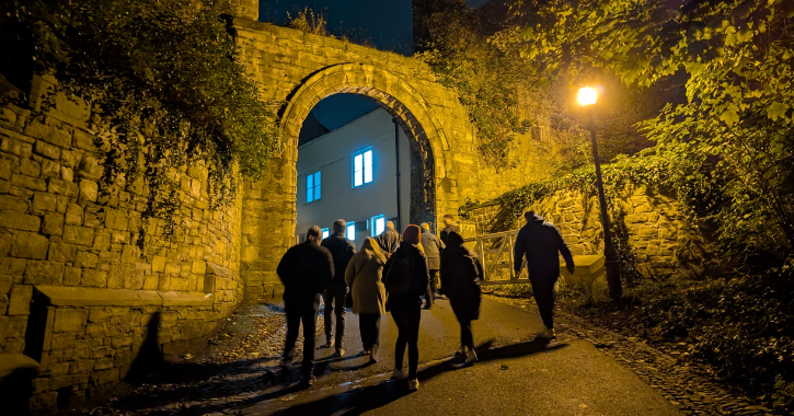 group of people walking through archway in Durham City at night.